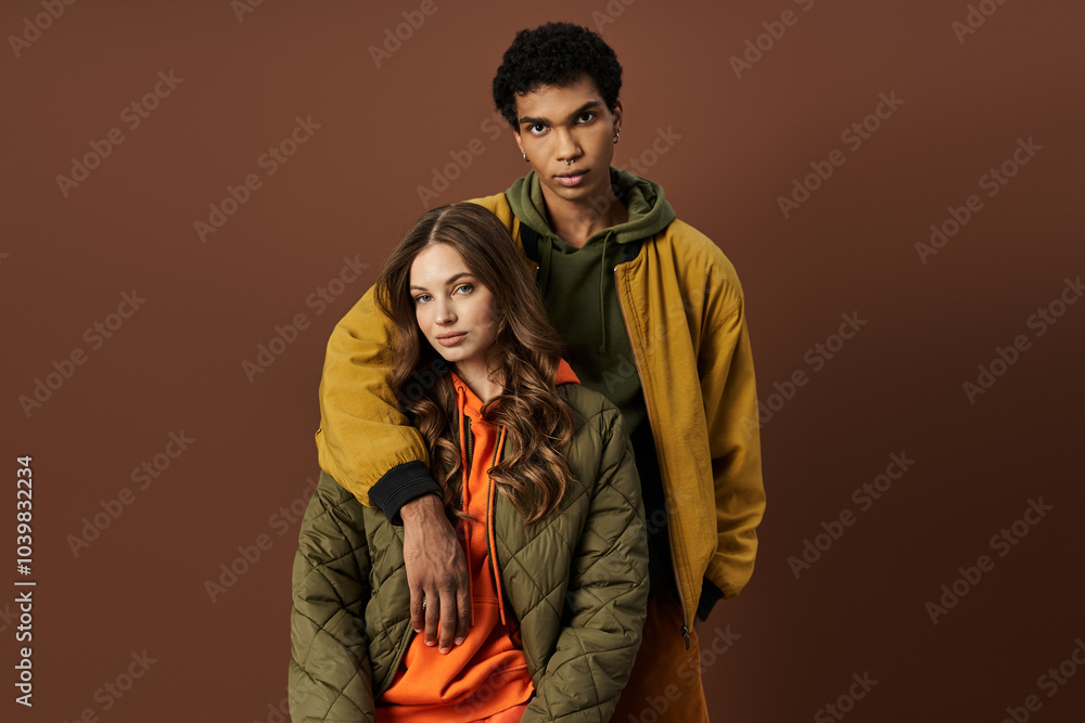 Fototapeta premium A fashionable couple showcases their stylish autumn attire against a rich, earthy background.