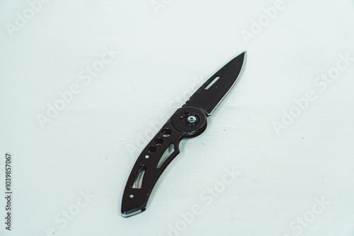 Mini size folding knife of solid black color partially opened isolated on white background. Close-up view of a black folding knife used for various outdoor or survival activities