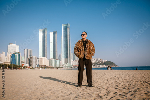 A Korean guy in a leopard fur coat walks along the beach against the backdrop of the autumn landscape of Busan Haeundae.