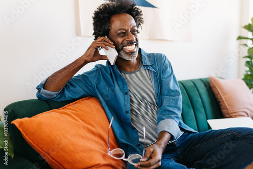 Happy mature man relaxing on a sofa, using his mobile phone to make a call