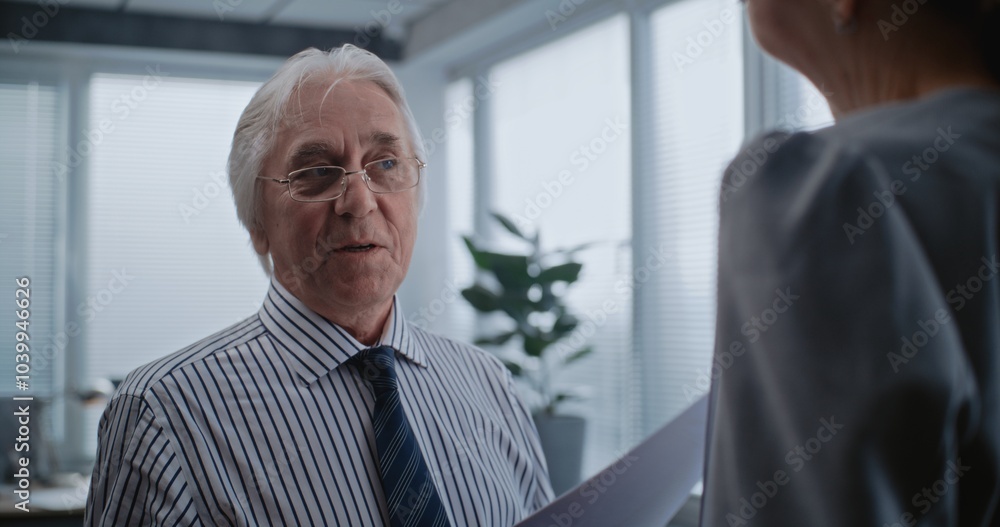 Obraz premium Senior boss of the company with papers talks to female financial specialist. Bank employee discuss business strategy with team leader. Modern office of international corporation. Business concept.