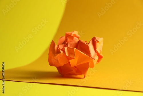 Orange crumpled paper on yellow background, closeup photo