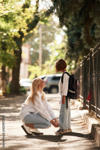 Side view. Schoolgirl with her mother are outdoors together