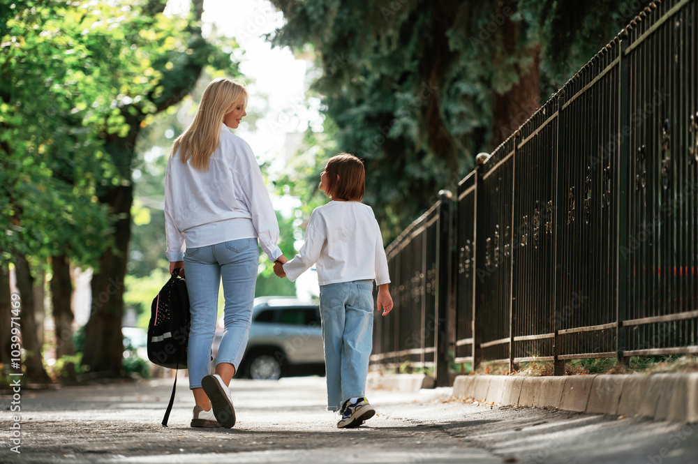 Rear view, walking. Schoolgirl with her mother are outdoors together Rear view, walking. Schoolgirl with her mother are outdoors together