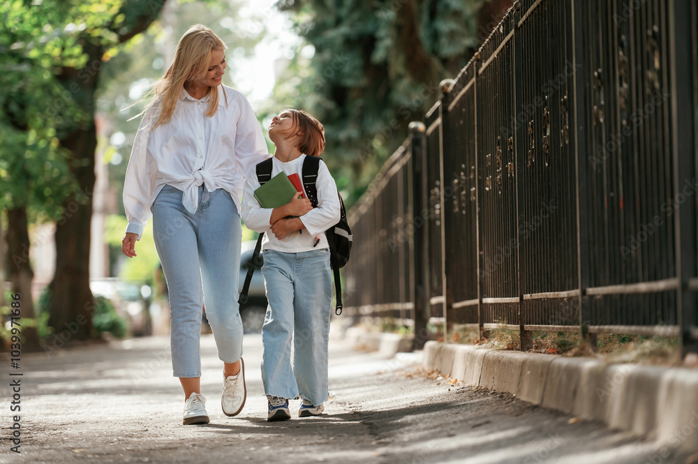 Obraz premium With books, front view. Schoolgirl with her mother are outdoors together