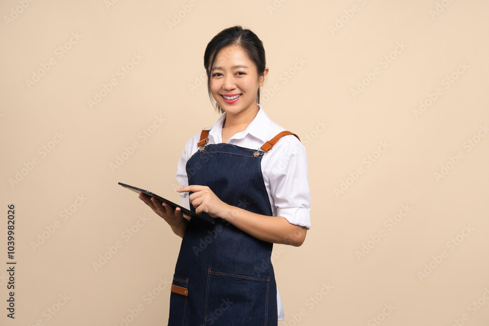 Smiling Asian female business owner wearing apron and holding tablet ready to take orders or manage food stock for coffee shop on white background Smiling Asian female business owner wearing apron and holding tablet ready to take orders or manage food stock for coffee shop on white background