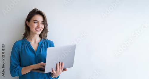 A smiling young woman with a laptop is standing against a gray background.