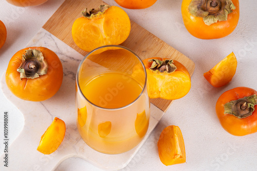 Fresh homemade persimmon juice in portioned glasses, with whole and cut persimmon c in the background