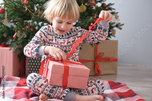 cute kid in Christmas pajamas opening gift box at christmas morning