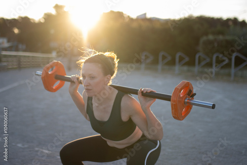 Young woman lifting weights exercising outdoors at sunset