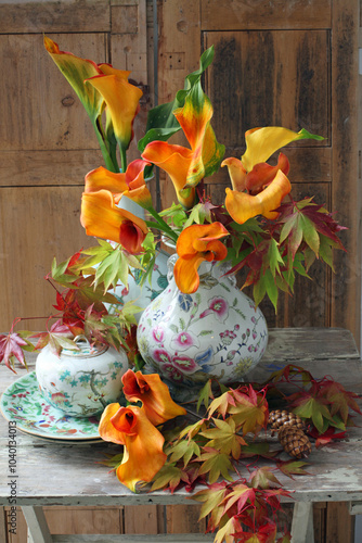 autumn still life of zantedeschia flowers in vases with maple leaves
