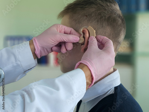 Audiologist fitting a young patient with a hearing aid in a clinical setting