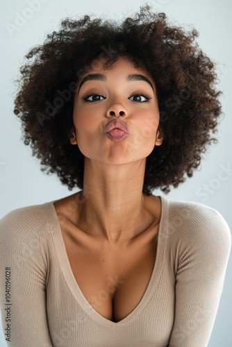 A woman with curly hair poses playfully in a neutral toned sweater against a ...