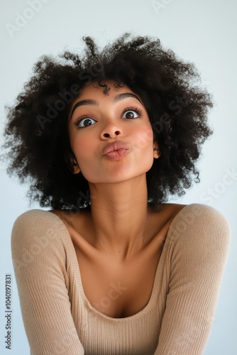 A woman with curly hair poses playfully in a neutral toned sweater against a ...