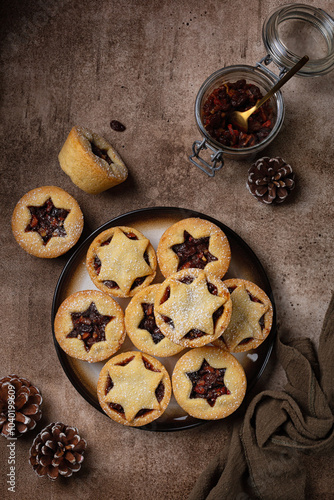 Brown food table with Traditional british christmas Mince pies on a brown plate, sprinkled with sugar. Also called mincemeat or fruit pie, filled with a mixture of fruit, spices and suet.