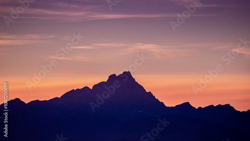 Silhouette of Monviso mountain at sunset with vibrant orange and purple hues in the sky. A dramatic and peaceful scene, perfect for nature, landscape, and mountain themes