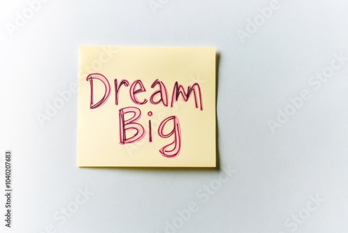 A sticky note displaying the inspirational phrase 'Dream Big' written in red on a pale yellow note placed against a plain white background, promoting motivation. photo