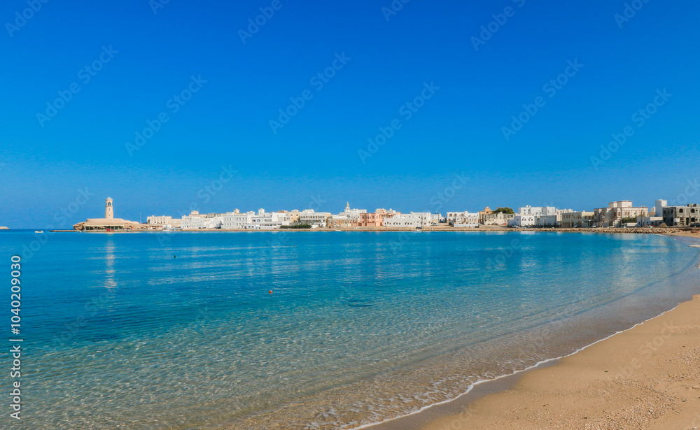 Coastal view of Sur Oman showcasing clear waters and vibrant architecture under a bright blue sky Coastal view of Sur Oman showcasing clear waters and vibrant architecture under a bright blue sky