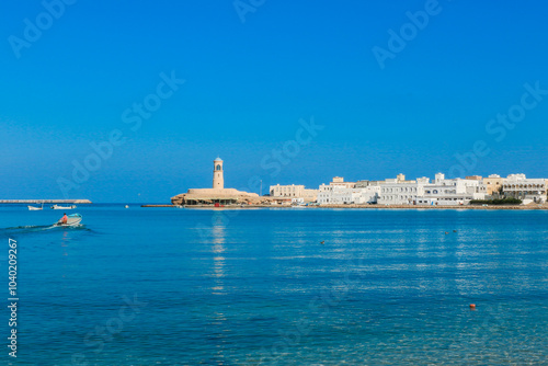 A serene view of the coastal town of Sur in Oman featuring a traditional boat on calm waters under a clear blue sky