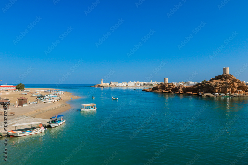 Beautiful coastal view of Sur in Oman showcasing boats anchored by golden sands under a clear blue sky Beautiful coastal view of Sur in Oman showcasing boats anchored by golden sands under a clear blue sky