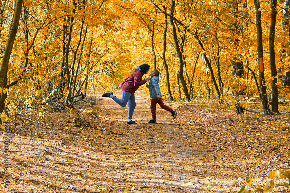 Obraz premium A woman and a son in autumn attire playfully posing in a forest with vibrant fall foliage.