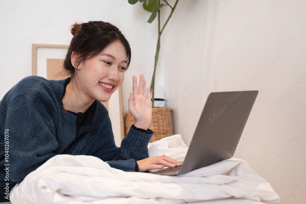 Relaxed Young Woman Using Laptop in Cozy Home Setting, Smiling and Waving, Casual Lifestyle, Remote Work or Online Communication