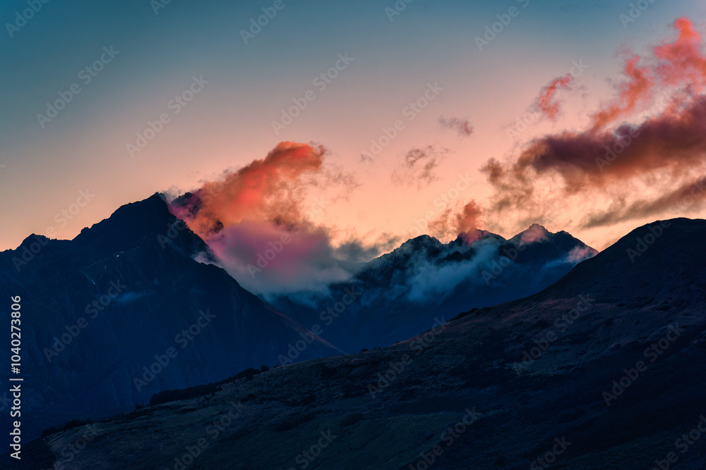 Fototapeta premium Mountain peak at sunset with colorful clouds flowing through