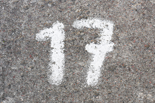 Number 17 painted on concrete. Numbered parking spot. Marked on ground with white paint. Parking lot numers background.