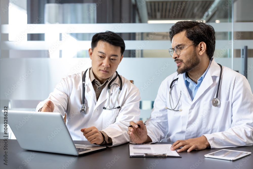 Doctors in formal attire collaborate using laptop in office, discussing patient details. Focus on teamwork, medical professionalism, digital communication. Healthcare professionals consulting Doctors in formal attire collaborate using laptop in office, discussing patient details. Focus on teamwork, medical professionalism, digital communication. Healthcare professionals consulting