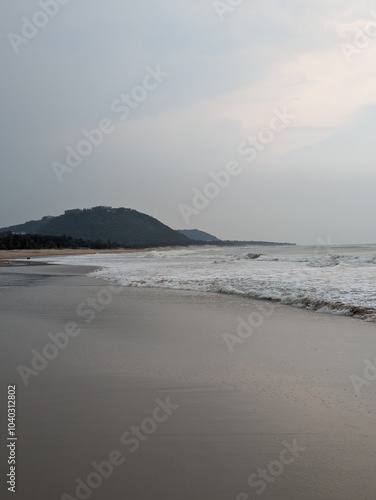 A serene evening at Rushikonda Beach, in Andhra Pradesh, India, with soft golden hues from the setting sun reflecting on the calm, blue waters. photo