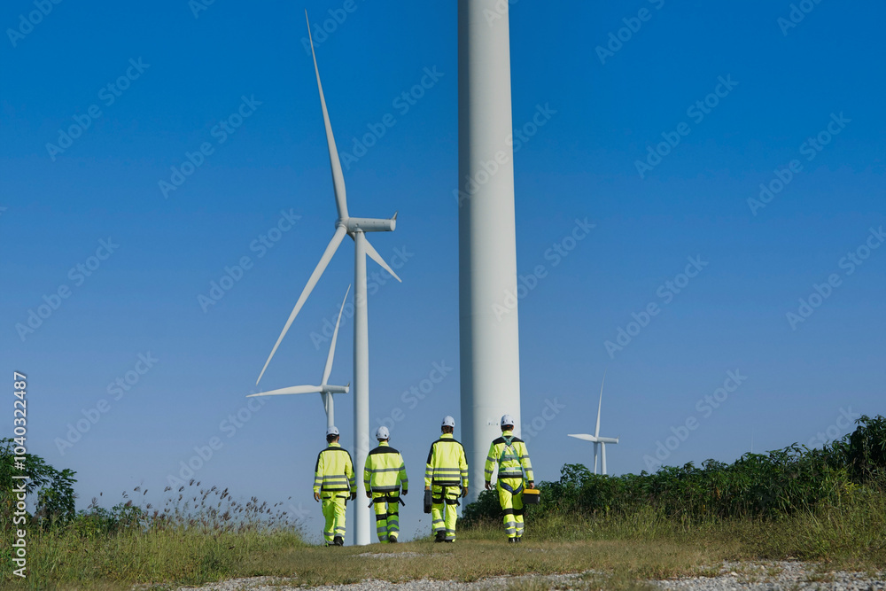 Team of male engineers in uniforms are walking around surveying and inspecting wind turbines. Wind turbine station brings wind to generate electricity. Clean energy concept.