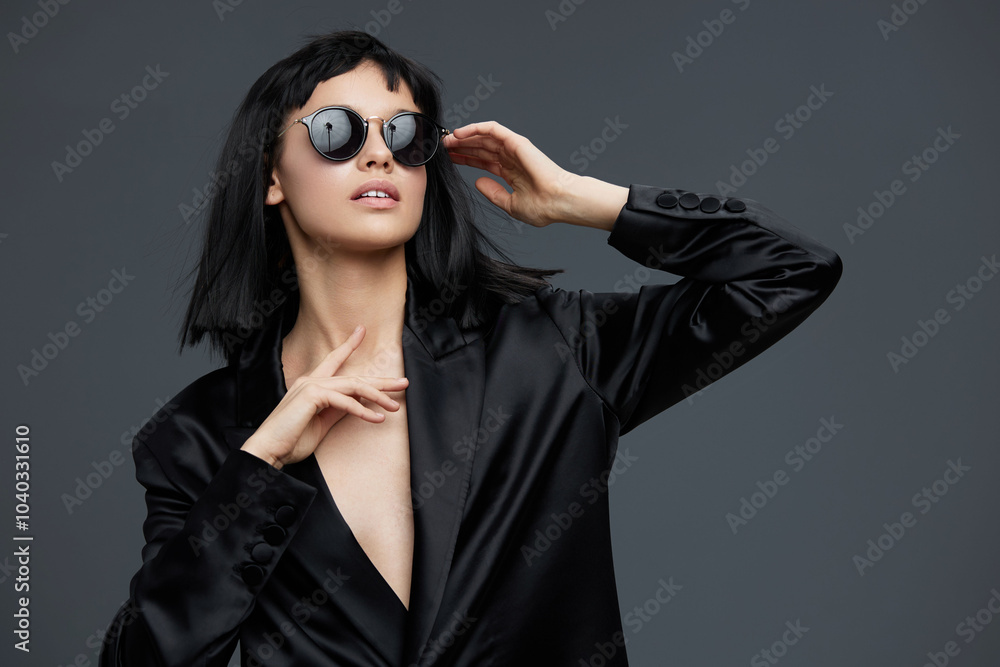 A woman in a black suit and sunglasses confidently poses for the camera on a gray background, embodying elegance and professionalism A woman in a black suit and sunglasses confidently poses for the camera on a gray background, embodying elegance and professionalism