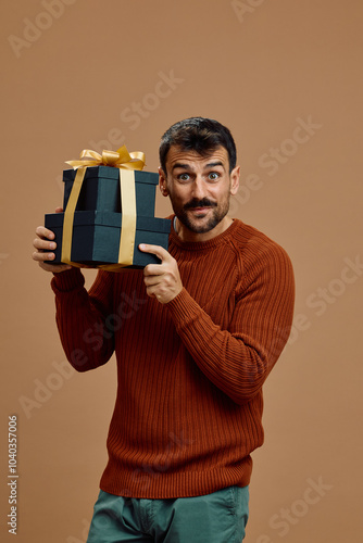 Surprised man holding black gift boxes with golden ribbon and looking at camera. photo