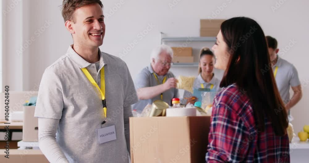 Smilling volunteer male worker giving a food and other stuff donation box to a happy grateful refugee woman at a social assistance center. Humanitarian help and social support concept. Smilling volunteer male worker giving a food and other stuff donation box to a happy grateful refugee woman at a social assistance center. Humanitarian help and social support concept.