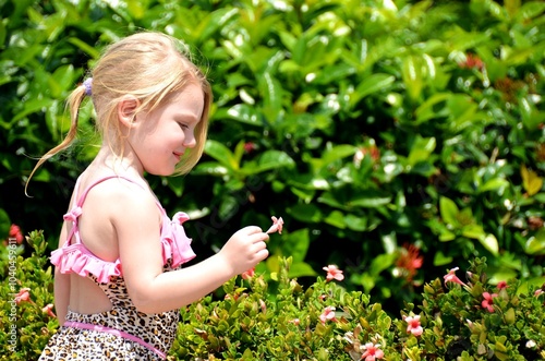 Criança usando roupas de banho, arrancando uma pequena flor de um jardim photo