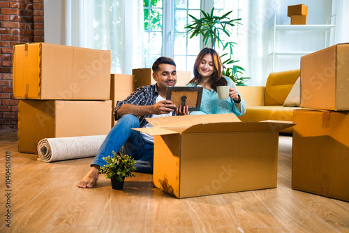 Indian Asian couple smiling while unpacking boxes in their new home, while looking at photo frame