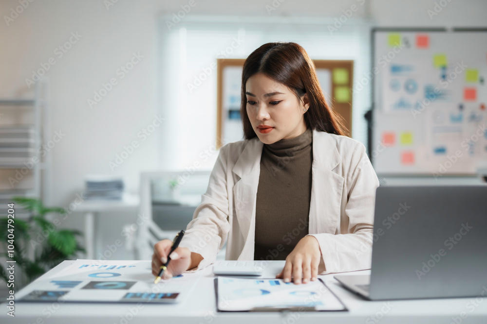 Focused businesswoman working with financial documents and using laptop while sitting at desk in modern office Focused businesswoman working with financial documents and using laptop while sitting at desk in modern office