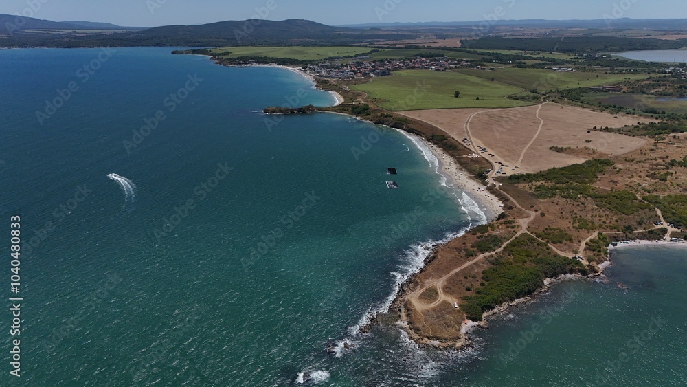 A stunning aerial view of a coastal landscape featuring a serene bay, vast green fields, and distant mountains under a clear blue sky. The image captures a peaceful seaside area with a few ships A stunning aerial view of a coastal landscape featuring a serene bay, vast green fields, and distant mountains under a clear blue sky. The image captures a peaceful seaside area with a few ships