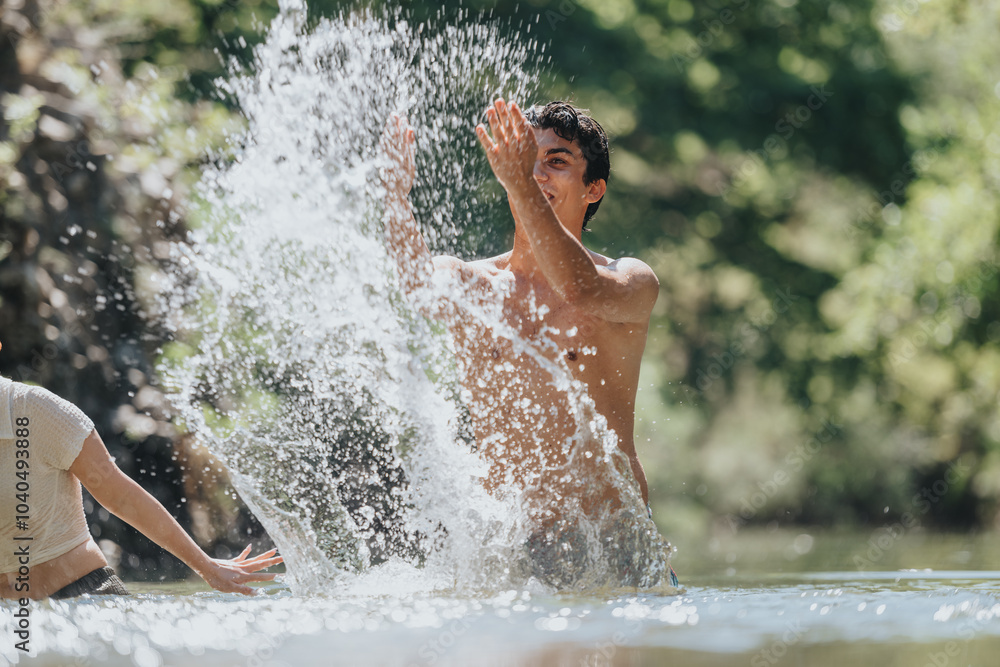 Fototapeta premium A young man energetically splashes water in a natural outdoor environment, expressing joy and freedom in the sunshine. The playful scene captures the essence of summer fun and relaxation.