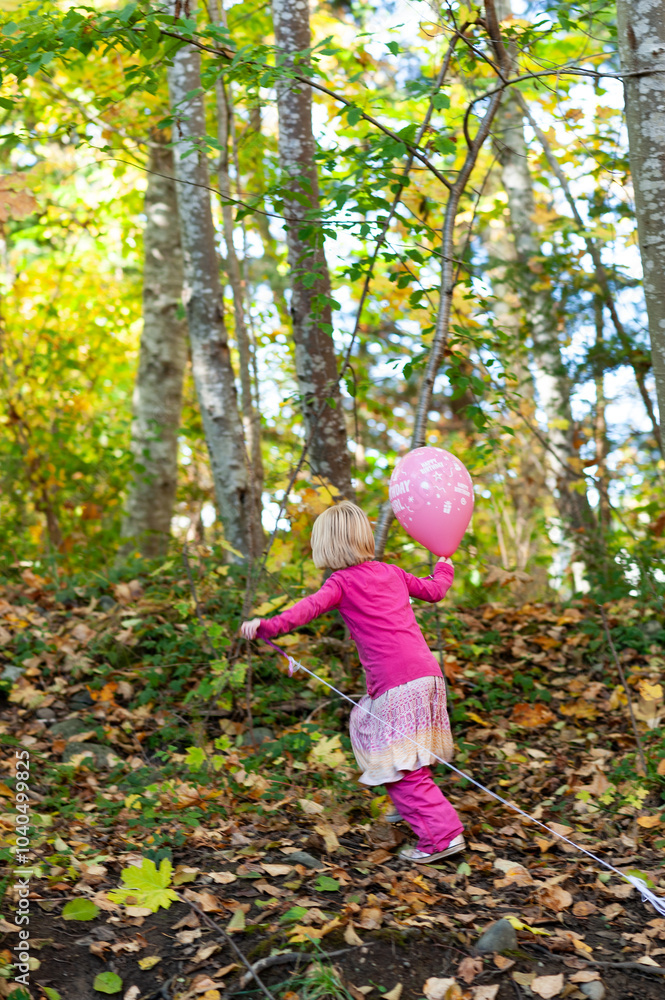 Young caucasian girl playing with a pink balloon on a long string in a park in autumn Young caucasian girl playing with a pink balloon on a long string in a park in autumn
