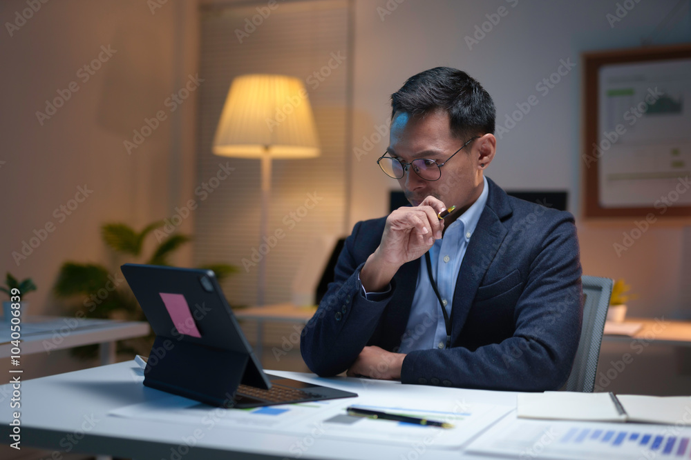 Businessman is working late, using a digital tablet and thinking about a solution for his business Businessman is working late, using a digital tablet and thinking about a solution for his business