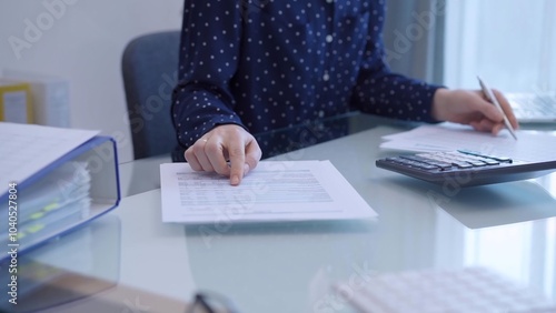 A female accountant with blue dotted blousy is using a laptop computer and calculator to calculate taxes at a glass desk in the office photo