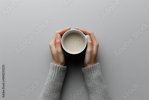Cozy hands holding a warm cup of coffee on a soft gray background in a comfor...