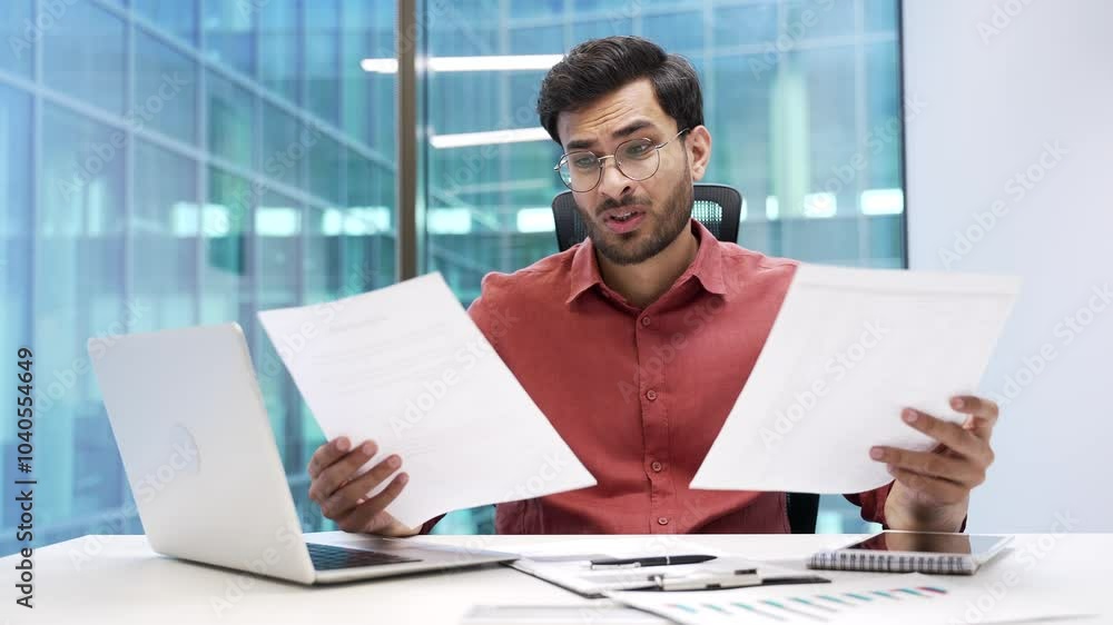 Confused businessman in glasses having difficulty with paper work sitting at workplace in business office. Puzzled entrepreneur looks at documents and cannot understand problem, looking at camera Confused businessman in glasses having difficulty with paper work sitting at workplace in business office. Puzzled entrepreneur looks at documents and cannot understand problem, looking at camera