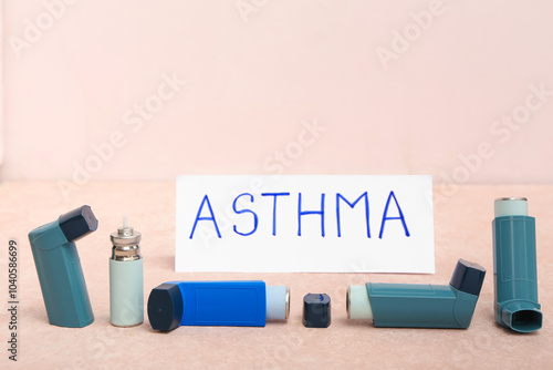 Modern inhalers and word ASTHMA on pink grunge table photo