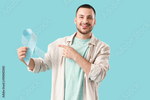 Young man pointing at blue ribbon on color background. Prostate cancer awareness concept