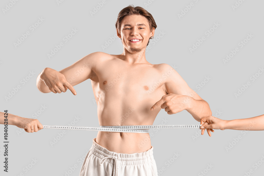 Female hands measuring young man's waist on light background. Weight loss concept Female hands measuring young man's waist on light background. Weight loss concept