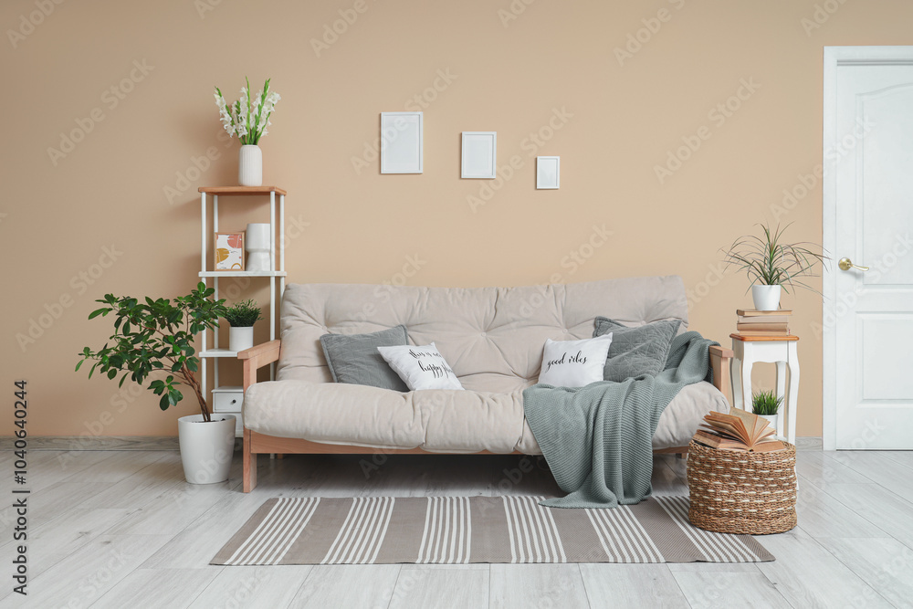 Fototapeta premium Sofa, decorated tree, shelving unit and pouf with book in interior of living room