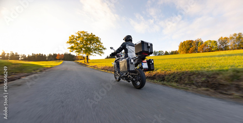 Driver riding motorcycle on empty road during sunset, autumn mountains