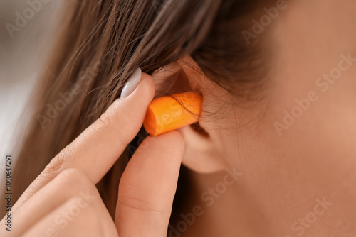 Young woman with ear plug in bedroom, closeup photo